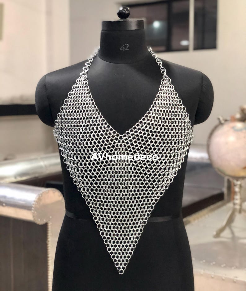 May include: A silver chainmail halter top displayed on a black mannequin. The top features a V-neck design and is constructed from small, interlocking metal rings. The mannequin is set against a neutral background.