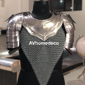 May include: A silver-colored medieval armor set, including a chest plate, shoulder guards, and chainmail. The armor is displayed on a black mannequin. The text "AVhomedeco" is visible on the chainmail.