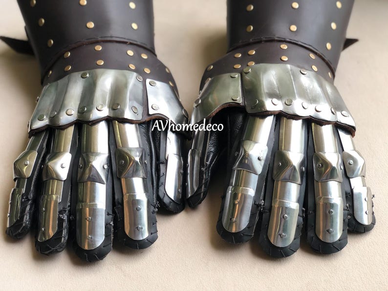 May include: Pair of medieval gauntlets. The gauntlets feature a combination of black leather and polished metal plates. The leather cuffs are adorned with small, gold-colored rivets. The metal plates articulate to allow for movement.
