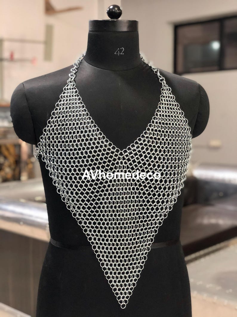 May include: A silver chainmail halter top with a V-neck design. The top is displayed on a black mannequin. The text "AVhomedeco" is visible on the front of the top. The mannequin has a black base and a black head.