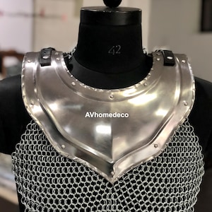 May include: A polished steel gorget, a piece of medieval armor, is displayed on a black mannequin. The gorget has a curved shape to protect the neck and upper chest, with a chainmail lower section. The brand name "AVhomedeco" is visible.