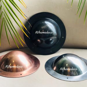 May include: Three metal dome-shaped objects with circular bases. One is black, one is copper-coloured, and the other is silver. Each has a rounded dome and a flat, circular base with evenly spaced holes. The text "AVhomedeco" is printed on each.