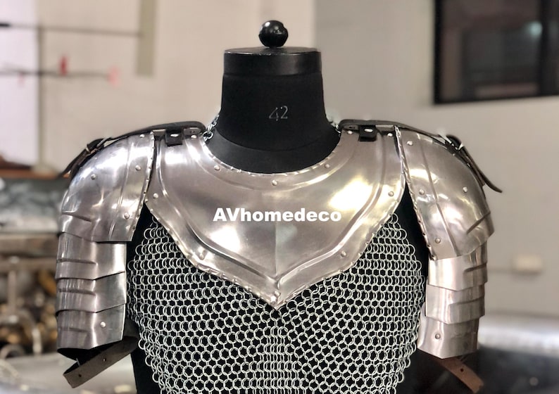 May include: A silver-colored metal chest and shoulder armor set, displayed on a black mannequin. The armor features layered shoulder plates and a chainmail shirt. The text "AVhomedeco" is visible on the chest plate.