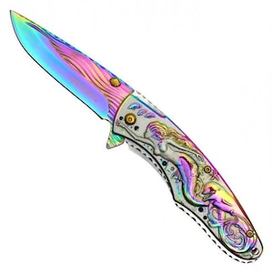 May include: A folding pocket knife with a rainbow-colored titanium finish blade and handle. The handle features an embossed silver-toned mermaid and dolphin design with iridescent accents. The blade has a curved edge and a pointed tip.