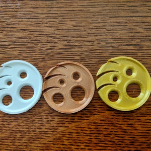 May include: Three round, 3D printed, plastic discs with a unique design. The discs are light blue, brown, and yellow.