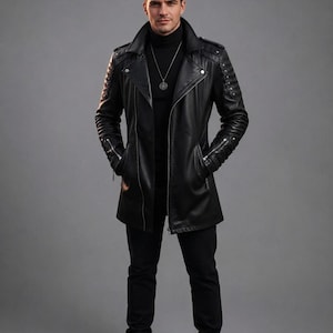 May include: A black leather trench coat featuring a wide collar, silver-tone zippers on the sleeves, and quilted shoulder and arm detailing. The coat is worn over a black turtleneck sweater and black trousers, paired with a silver pendant necklace.