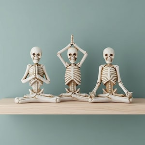 Peut inclure: Trois figurines de squelettes blanc cassé en poses de yoga sont posées sur une étagère en bois sur un fond turquoise. Chaque squelette est dans une asana différente, avec les bras levés ou les mains en position de prière. Les figurines sont détaillées.