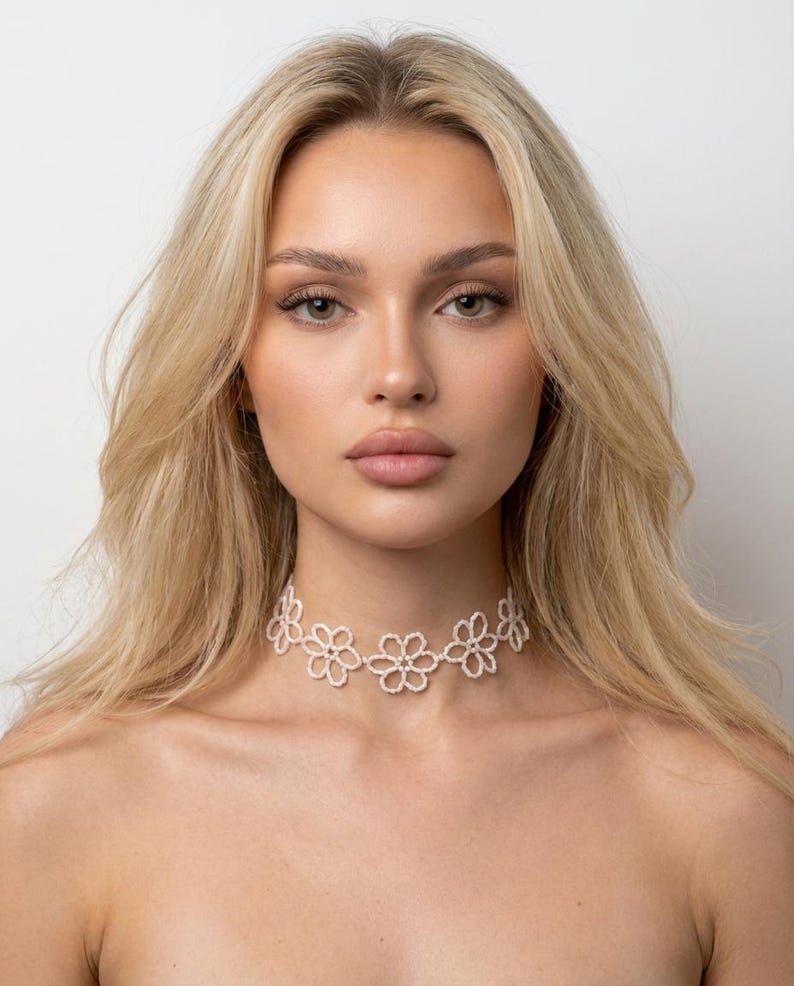 May include: A white floral choker necklace. The necklace features a series of delicate, openwork flower designs. The choker is worn around the neck and is a stylish accessory.