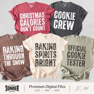 May include: Five short-sleeved crew neck t-shirts in red, dark gray, brown, cream, and sage green. Each shirt features distressed white or black text: Christmas Calories Don't Count, Cookie Crew, Baking Through The Snow, Baking Spirits Bright, and Official Cookie Tester.