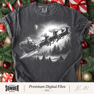 May include: Dark gray t-shirt featuring a black and white graphic of Santa Claus in a sleigh pulled by reindeer, flying in front of a full moon. The shirt includes the text "Premium Digital Files" and "N. 101".
