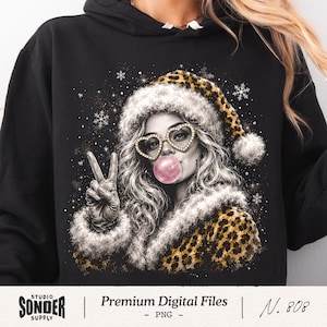 May include: A black hooded sweatshirt featuring a graphic print of a person wearing a leopard print Santa hat and heart-shaped glasses, blowing a pink bubblegum bubble, and making a peace sign gesture, surrounded by white snowflakes.