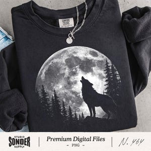 May include: Black sweatshirt featuring a graphic of a howling wolf in silhouette against a full moon and pine trees. A silver necklace with a pendant is draped on the sweatshirt. The sweatshirt has a Comfort Colors label.