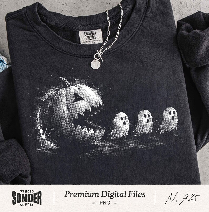 May include: A black crewneck sweatshirt featuring a white graphic print of a large carved jack-o'-lantern pumpkin with a jagged mouth chasing three small ghosts. The garment has a Comfort Colors brand label at the inner neckline and a silver chain.