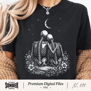 Peut inclure: T-shirt noir avec une illustration romantique de deux squelettes s'embrassant sous un croissant de lune et des étoiles. Les squelettes sont entourés de fleurs. Le texte "Premium Digital Files - PNG - N. 505" est en bas.