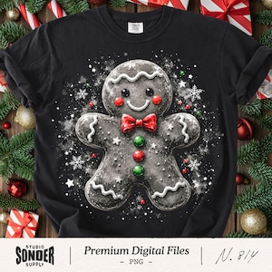 May include: A black t-shirt featuring a central graphic of a dark gingerbread person with white icing details, a red bow tie, and three round buttons in red and green. The design is surrounded by white snowflakes and small colorful dots.
