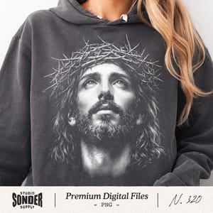 Peut inclure: Un sweat-shirt à capuche gris anthracite arborant une impression graphique blanche détaillée représentant un personnage barbu portant une couronne d'épines, les yeux tournés vers le haut. Le motif est centré sur la poitrine.