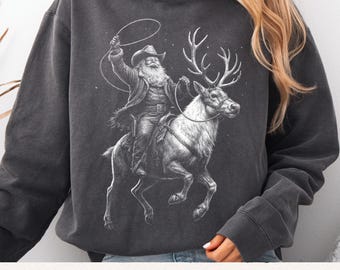 May include: Dark gray hoodie featuring a black and white illustration of Santa Claus riding a reindeer and holding a lasso. The image has a vintage, distressed look. The text "Premium Digital Files" is at the bottom.