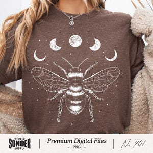 May include: A brown t-shirt featuring a detailed white illustration of a bee with outstretched wings, set against a backdrop of crescent moons and stars. The text "Premium Digital Files - PNG - N. 401" is at the bottom.