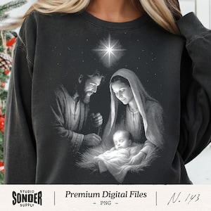 May include: A charcoal gray crewneck sweatshirt featuring a white graphic print of the Nativity scene. The design depicts a bearded figure and a veiled figure looking down at an infant in a manger, illuminated by a bright star above them.