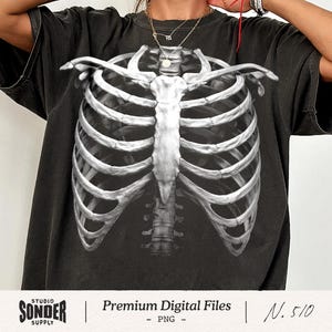 May include: Black t-shirt featuring a detailed, grayscale illustration of a human rib cage. The design is centered on the shirt, with the rib cage extending from the shoulders to the lower chest. The shirt has a vintage, worn look.