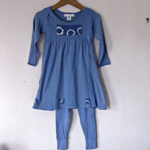 May include: A blue long-sleeved dress with a white and blue patterned design on the bodice. The dress is paired with matching blue leggings.