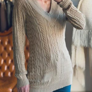 May include: A white ceramic mug with a black handle and the text "But First, Coffee" in a bold, black font. The mug is set against a blurred background, suggesting a cozy setting.