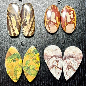 May include: Four pairs of polished gemstones in various shapes and colors. Pair A features brown and tan striped patterns. Pair B has red and cream patterns. Pair C displays yellow and green patterns. Pair D shows white and maroon patterns.