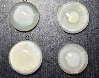 May include: Four circular, translucent cabochons with swirling white and cream patterns. Each cabochon features a unique design, with variations in the density and arrangement of the internal swirls. The cabochons are set against a dark background.