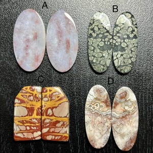 May include: Four pairs of polished gemstones, each with unique patterns and colors. Pair A features oval stones with red and white patterns. Pair B has green and black speckled stones. Pair C displays rectangular stones with yellow, red, and cream patterns. Pair D shows oval stones with brown and white swirls.