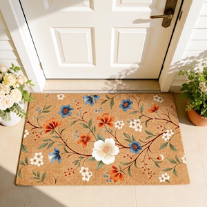 Peut inclure: Un paillasson rectangulaire avec un motif floral. Le tapis présente un fond beige avec un motif de fleurs orange, bleues et blanches et de feuilles vertes. Le tapis est placé devant une porte blanche.