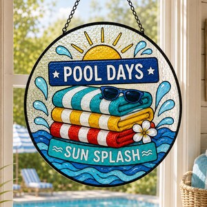 May include: A circular stained glass suncatcher featuring a yellow sun, blue water splashes, and a stack of teal, yellow, and red striped towels topped with black sunglasses. The text reads POOL DAYS and SUN SPLASH in bold white lettering.
