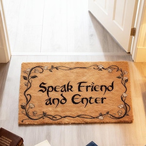 Könnte beinhalten: Rechteckige Fußmatte mit dem Schriftzug "Speak Friend and Enter" in schwarzer Schrift. Die Matte ist beige mit einem dekorativen Rand aus Ranken und Blumen. Sie liegt vor einer weißen Tür.
