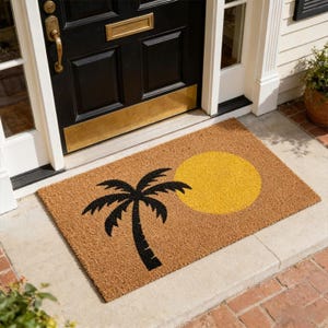 Puede incluir: Una alfombra rectangular con un fondo marrón presenta un diseño de palmera negra y sol amarillo. La alfombra está colocada frente a una puerta negra con detalles dorados y un marco de puerta blanco.