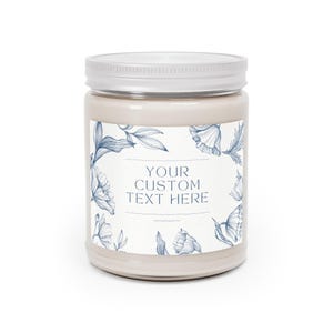 Puede incluir: Un tarro de vela beige con tapa blanca. El tarro tiene una etiqueta con ilustraciones florales azules y el texto "YOUR CUSTOM TEXT HERE". La vela es un art&iacute;culo decorativo.