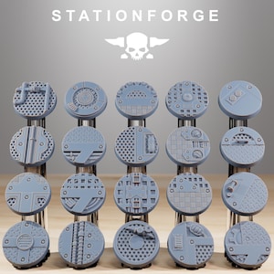Puede incluir: Una colección de bases en miniatura circulares grises con varios diseños industriales. Las bases están dispuestas en filas y columnas, mostrando diferentes texturas y patrones. El texto "STATIONFORGE" y un logotipo de calavera son visibles en la parte superior.
