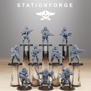 Puede incluir: Colección de figuras en miniatura grises de soldados, cada uno con un arma. Las figuras están sobre bases circulares negras, dispuestas sobre soportes de vidrio transparente. La palabra "STATIONFORGE" y un logotipo de calavera están impresos en la parte superior.