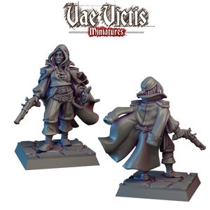 Puede incluir: Dos figuras en miniatura grises de una persona con abrigo largo y capucha, sosteniendo una pistola. Las figuras están sobre una base cuadrada. El texto "Vae Victis Miniatures" está en la parte superior.