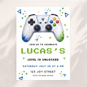 May include: A white invitation card featuring a watercolour video game controller with blue and green paint splatters. Text reads: JOIN US TO CELEBRATE LUCAS'S LEVEL 10 UNLOCKED SATURDAY JULY 25 AT 4 PM 123 JOY STREET RSVP TO 9680 00000 with geometric shapes.
