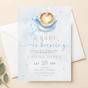 Pode incluir: Convite para chá de bebé com design em aquarela. O convite apresenta uma xícara de café com um desenho em forma de coração na espuma, uma fita azul e o texto "A BABY is brewing". Os detalhes incluem a data, hora e local.