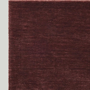 May include: A close-up of a burgundy-colored rug with a textured surface. The rug has a soft, plush appearance and a rectangular shape. The color is a deep, rich shade of red-brown.