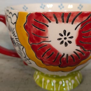 May include: A red and yellow floral patterned ceramic mug with a red handle and a green base.