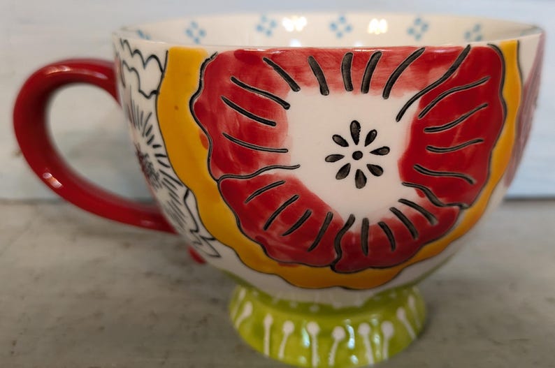 May include: A red and yellow floral patterned ceramic mug with a red handle and a green base.