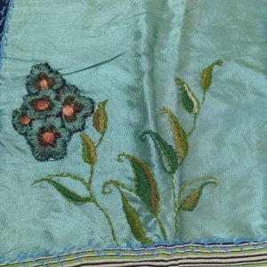 May include: A turquoise blue fabric with a green and brown embroidered floral design. The fabric is sewn to a green and white striped fabric.