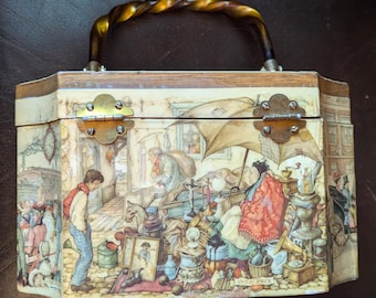 May include: Vintage decorative box with a detailed illustration of a street scene, featuring a twisted handle and brass hardware. The box depicts a bustling market with various items and figures, showcasing a unique artistic style.