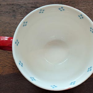 May include: A red ceramic teacup with a white interior and blue floral pattern.