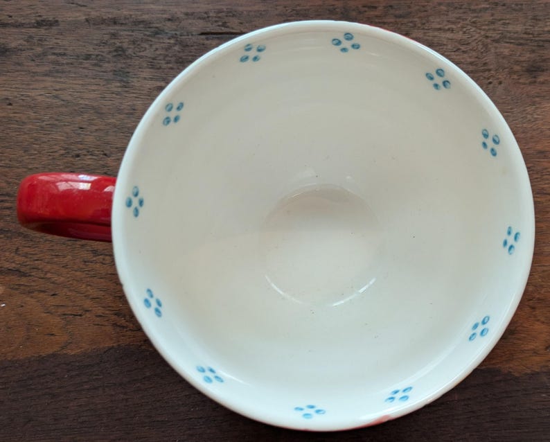 May include: A red ceramic teacup with a white interior and blue floral pattern.