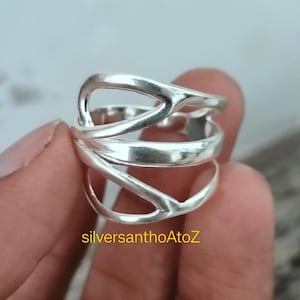 以下が含まれることがあります： ユニークなオープンデザインのシルバーリング。リングは複数のバンドが交差しており、人目を引くレイヤード効果を生み出しています。光沢のある磨かれた金属で作られたリングは、ジュエリーのステートメントピースです。