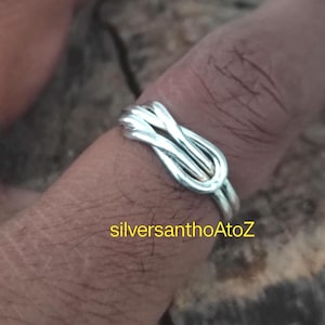 May include: A silver ring featuring a knot design. The ring is worn on a finger. The image includes the text "silversanthoAtoZ".