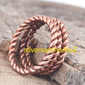 Op de afbeelding: Een koperkleurige ring met een gedraaid touwontwerp. De ring is gemaakt van meerdere strengen metaal die tot een getextureerd oppervlak zijn gedraaid. De tekst "silversanthoAtoZ" is zichtbaar op de ring.