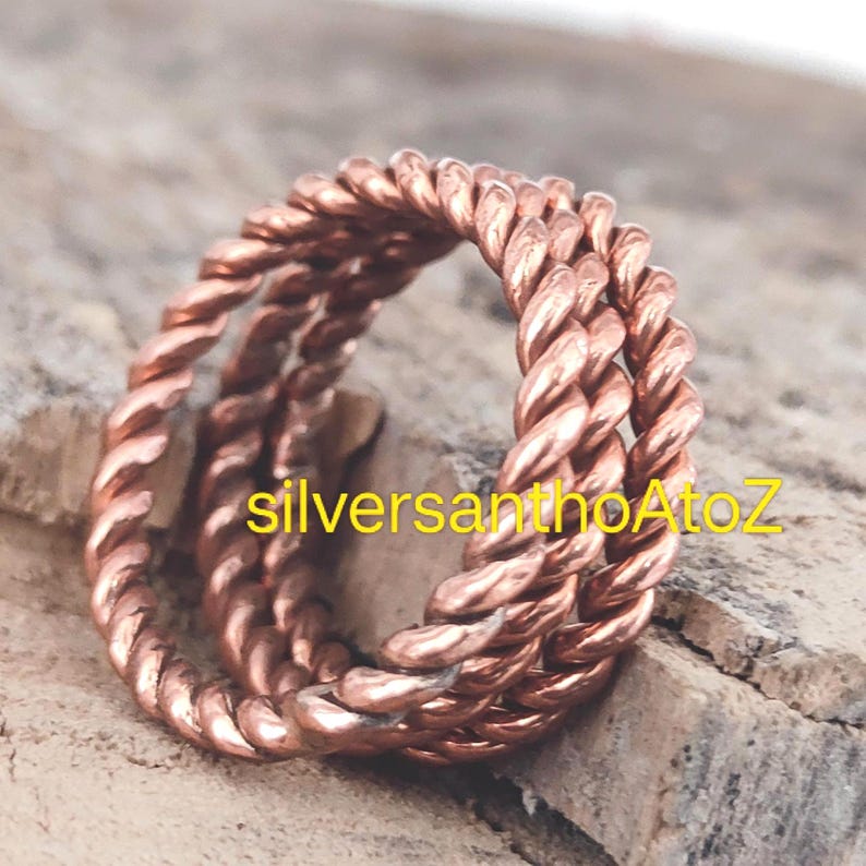 Op de afbeelding: Een koperkleurige ring met een gedraaid touwontwerp. De ring is gemaakt van meerdere strengen metaal die tot een getextureerd oppervlak zijn gedraaid. De tekst "silversanthoAtoZ" is zichtbaar op de ring.